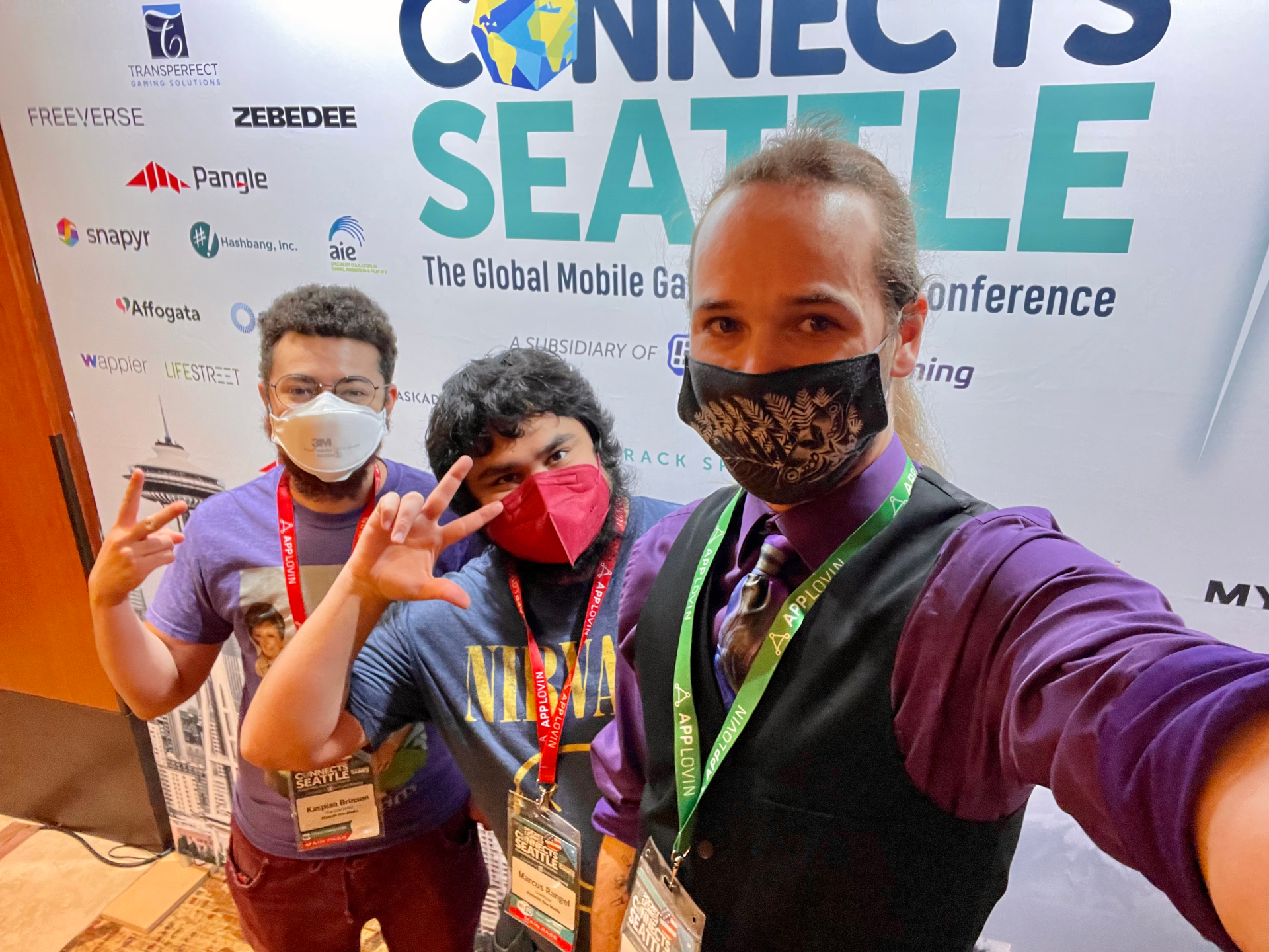 Kaspian, Salem, and Joshua wearing masks in front of the Pocket Gamer Connects 2022 sign