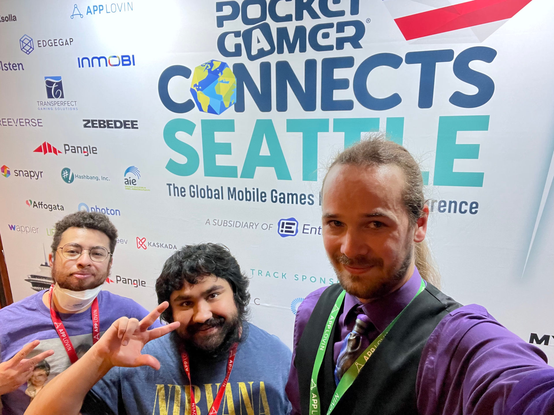 Kaspian, Salem, and Joshua wearing masks in front of the Pocket Gamer Connects 2022 sign